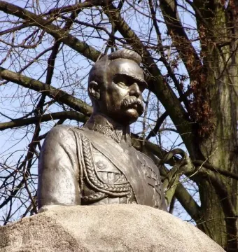 Bronze bust of Józef Piłsudski in military uniform on a stone base against a blue sky.