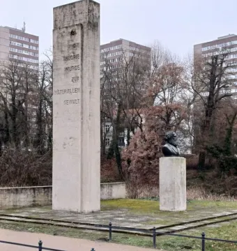 Karl Marx Monument showing a dark bust of a bearded man beside a tall stone stele with German text.