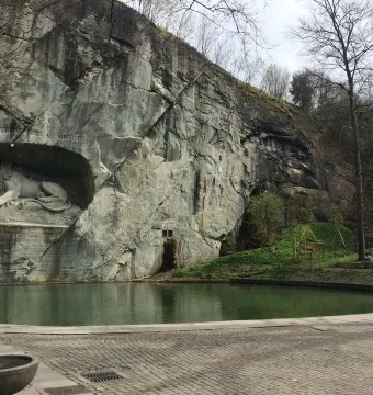 The Lion Monument in Lucerne carved into a rock face beside a reflective pond and paved walkway.
