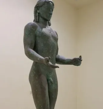 The Piraeus Apollo bronze statue with long braided hair and green patina, standing on a stone plinth.