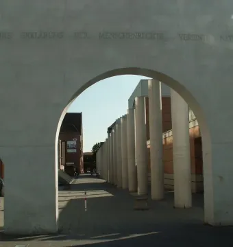 The Way of Human Rights concrete archway with engraved German text, framing a walkway lined with tall concrete pillars.