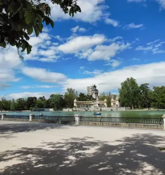 The Alfonso XII Monument rises across a lake, with an equestrian statue atop the monument and colonnades on the far shore.