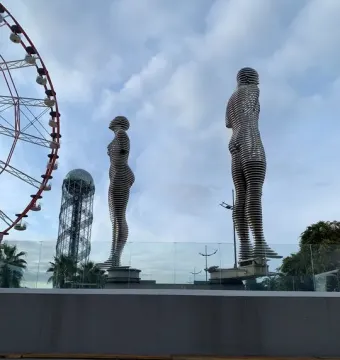 Ali and Nino sculpture with two slatted human figures facing each other, with a ferris wheel and spiral tower in the background.