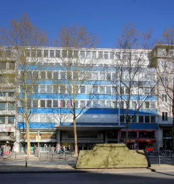 Ruhender Verkehr, a large concrete sculpture shaped like a sedan, stands on a sidewalk in front of an urban building.