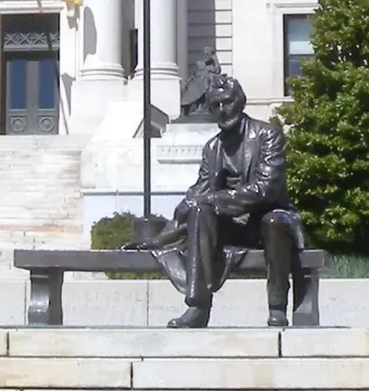 Seated Lincoln sculpture of a bearded man in a suit beside a stone courthouse with columns and steps.