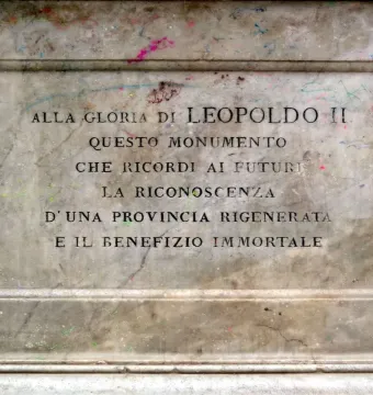 Weathered stone panel from the Canapone monument with an Italian inscription carved into a recessed section and colorful splatters on the surface.
