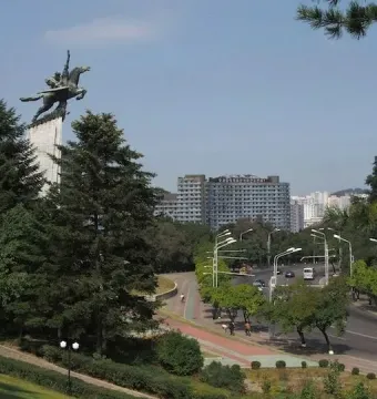 Chollima Statue of a winged horse with two figures on a tall pedestal, surrounded by trees and city buildings.