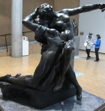 The Eternal Springtime bronze sculpture of a man embracing a woman, displayed on a pedestal in a museum gallery.