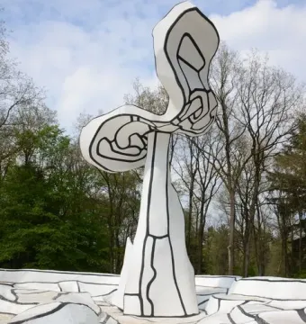 Jardin d\'émail sculpture with white abstract forms, black outlines, and tiered steps against trees and a cloudy sky.