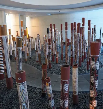 Aboriginal Memorial installation with numerous decorated cylindrical poles in a modern gallery space.