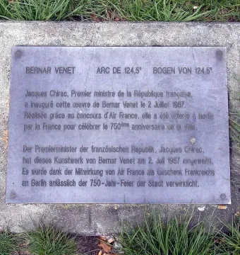 Metal plaque for Bernar Venet’s Arc de 124,5° set into a weathered concrete base in the grass.