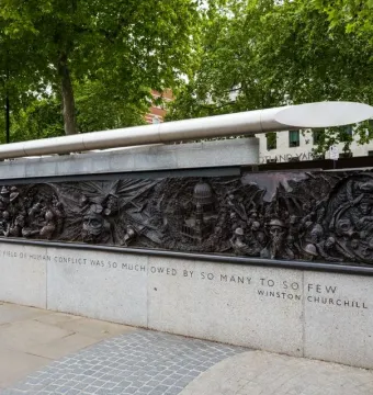 Battle of Britain Monument bronze relief panel with figures, a domed building under attack, and a Churchill quote on the stone base.
