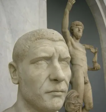 White marble bust of Philip the Arab with close-cropped hair and a short beard, shown with a blurred statue in the background.