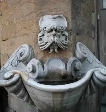 Fontana dello Sprone stone fountain with a carved bearded face spouting water into an ornate marble basin.