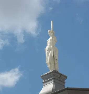 Girl with an Oar statue seen from below against a blue sky with clouds.