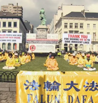 The John Cockerill Monument stands in a Brussels square with demonstrators gathered on the grass in front of it.