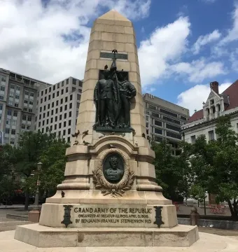 Stephenson Memorial, a tall stone obelisk with bronze figures, including two uniformed men holding a flag and a bust in a circular frame.
