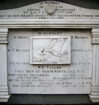 Titanic Musicians\' Memorial plaque with a central mourning figure and engraved names on a brick wall.