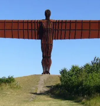 The Angel of the North sculpture stands on a grassy hill with outstretched wings under a clear blue sky.