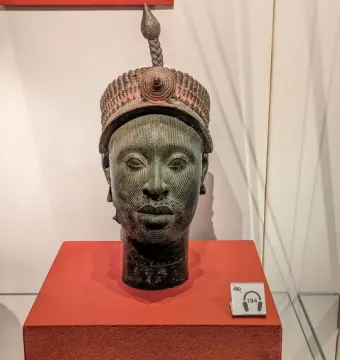 Bronze Head from Ife with green patina and intricate facial markings on a reddish pedestal.