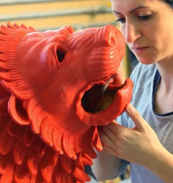 A woman works on the open mouth of the Chimera of Arezzo sculpture with a slender tool.