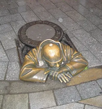 Čumil bronze sculpture of a man emerging from a manhole on a wet street