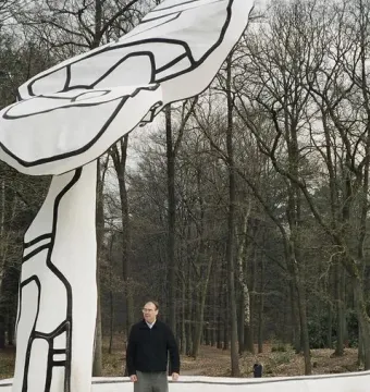 Jardin d\'émail sculpture with a man standing on its white, black-outlined surface in a bare forest