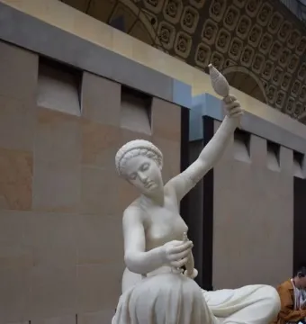 Jeune fille de Mégare, a white marble statue of a seated young woman spinning with a spindle and distaff.