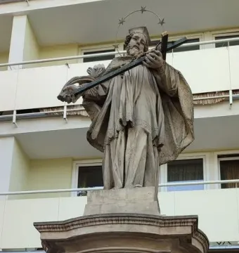 John of Nepomuk statue holding a crucifix on an ornate pedestal with a star-studded halo behind his head.
