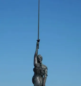 Verity sculpture seen from behind, holding a raised sword and scales against a blue sky.
