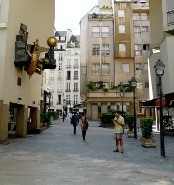 The Defender of Time clockwork sculpture on a building wall in Paris, showing a golden beast, a sphere, and a small sword-bearing figure.