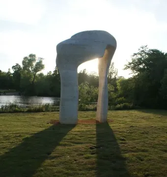 Henry Moore\'s The Arch standing on a grassy lawn with the sun shining through its opening and long shadows stretching across the grass.