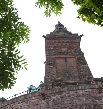 Kyffhäuser Monument seen from below, framed by green trees against a clear sky.
