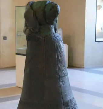 Napir-Asu statue seen from the back and right side, with a long draped garment and dark patinated surface.
