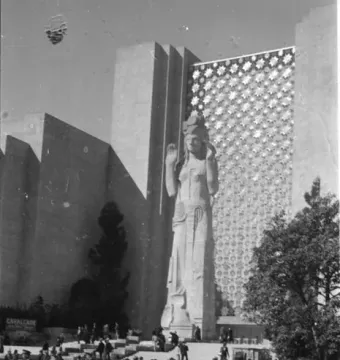 Pacifica statue stands before a geometric exhibition building with crowds gathered around the base.