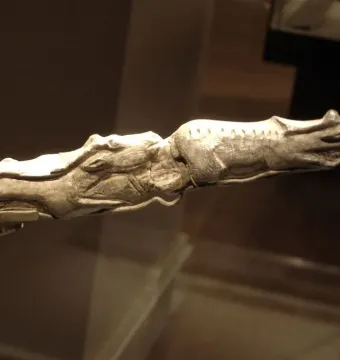 Elongated ivory carving of two swimming reindeer on a metal stand.