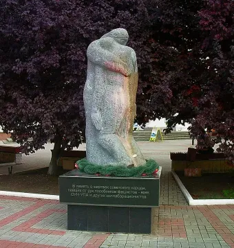 The Shot in the Back monument showing two stone figures on a dark base with Cyrillic text, set among trees and paved paths.
