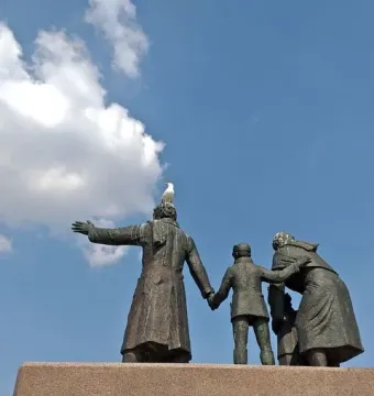 Auswandererdenkmal sculpture group on a tall granite pedestal, with a seagull perched on the central figure\'s head.