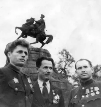 Upper portion of the Monument to Bohdan Khmelnytsky with a rider on a rearing horse above a rocky pedestal, partly obscured by three men in the foreground.