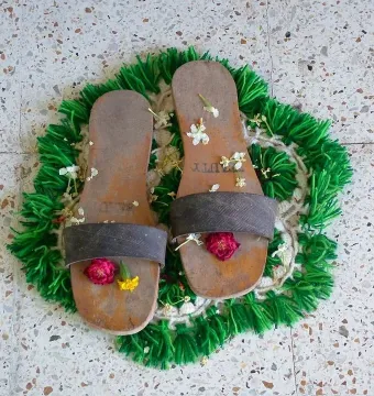 Charan Paduka sandals adorned with flowers on a green mat.
