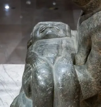 Close-up of the Las Limas Figurine showing a squat carved figure with a broad face and detailed chest designs, held by part of a larger figure.