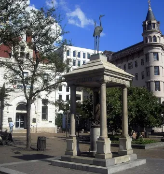 Temperance Fountain in a city square, with a stone pavilion and bird statue above it.