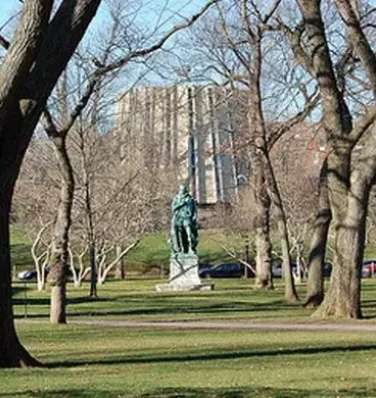 William the Silent bronze statue on a stone base in a grassy setting with leafless trees and a large building in the background