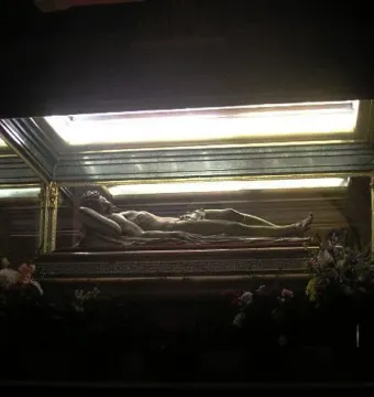 Cristo Yacente reclining in a glass display case with flowers below