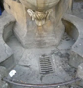 Lower section of Fontana dello Sprone with a grotesque face spouting water into a circular marble basin.