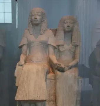 Horemheb and Amenia seated side by side on a stone bench, with their hands joined in the center.
