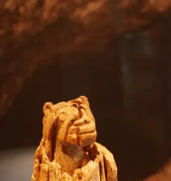 Lion-man sculpture with an animal-like head, upright body, and visible fractures in the aged material.