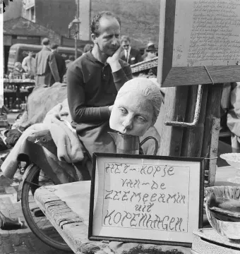 Detached head of The Little Mermaid resting on a metal pitcher beside a framed sign reading \