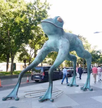 Lucky Frog sculpture with a turquoise-green patina and golden eyes on a sidewalk.
