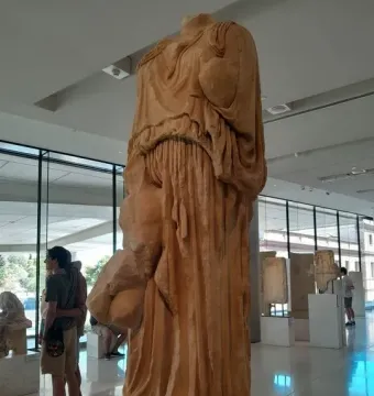 Headless marble statue of Procne and Itys on a white pedestal in a museum gallery.